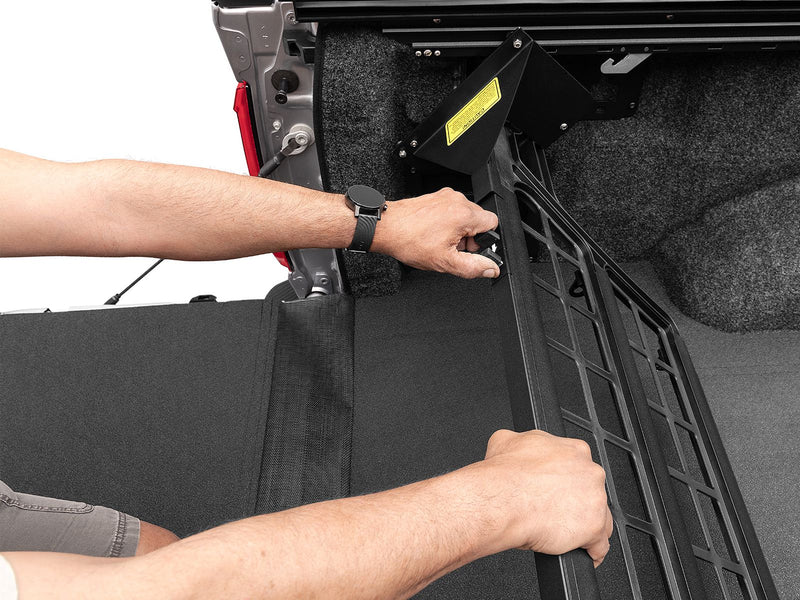 Hands swinging the Roll-N-Lock Cargo Manager up from its stowed position with a tonneau cover part drawn above