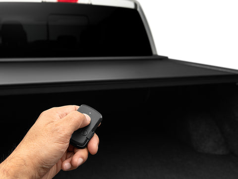 A hand pressing the Roll-N-Lock E-Series two-button wireless key fob with the powered cover closed behind it
