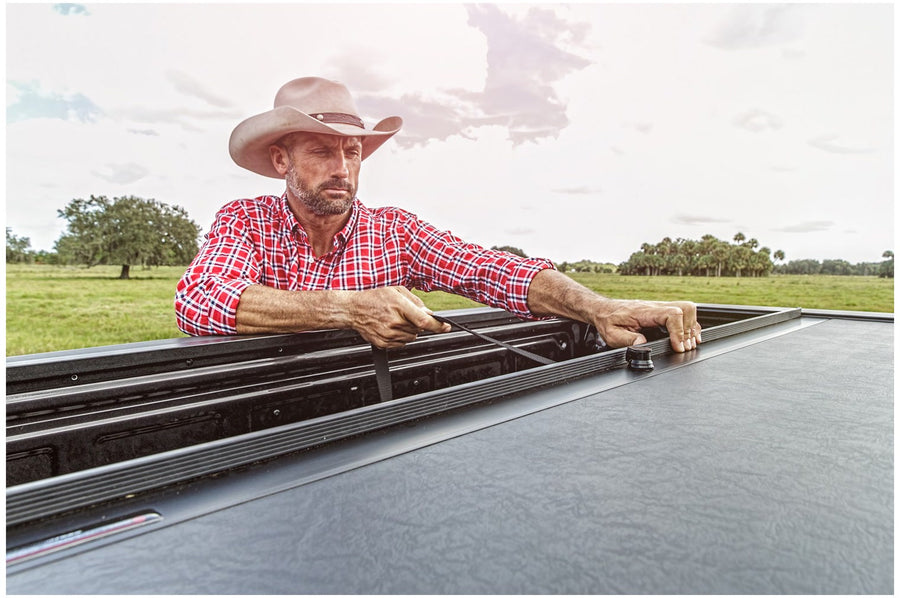 Roll-N-Lock M-Series retractable tonneau cover rolled open, a man reaching into the fully accessible truck bed in an open field