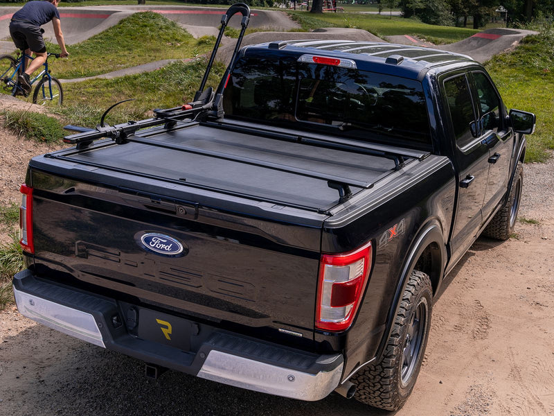 Roll-N-Lock M-Series XT closed on a 2021-2026 Ford F-150 with a bike carried on the MaxTrak T-slot rails at a gravel trailhead