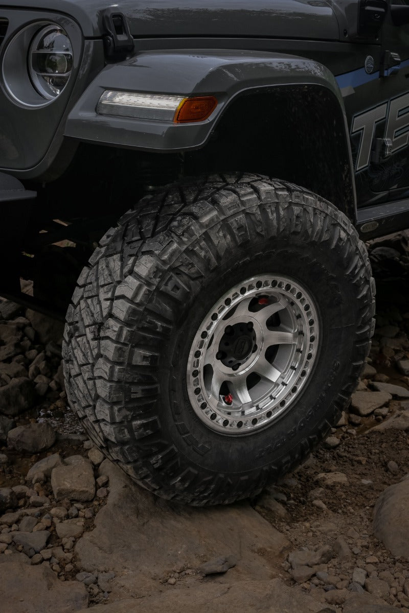 TeraFlex Olympus beadlock off-road wheel with a machined finish on the front corner of a gray lifted 4x4 on rocks, with a mud-terrain tire