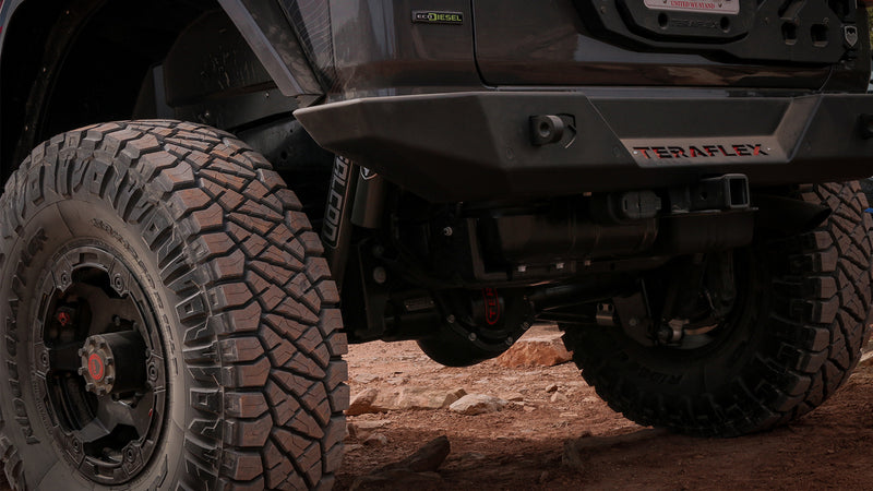 TeraFlex Rear Bumper on a Jeep Wrangler: rear corner of gray Jeep Wrangler JL EcoDiesel with TeraFlex bumper and Falcon shock on dirt trail