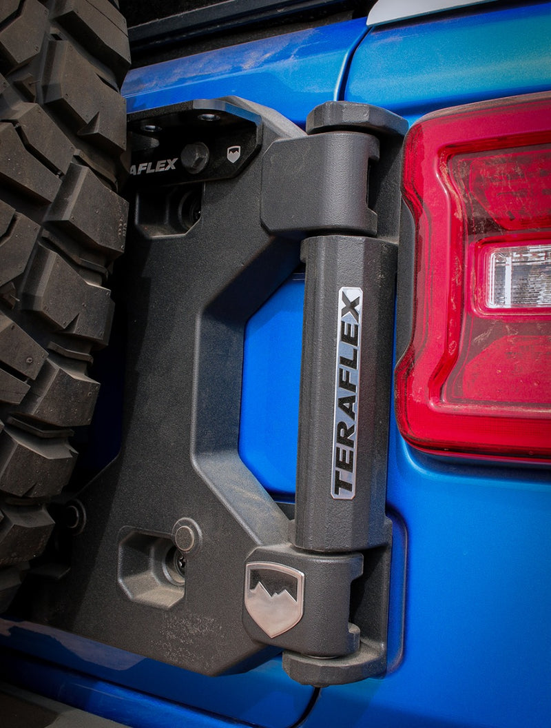 Close-up of the TeraFlex Tire Carrier & Tailgate Accessory: close-up of TeraFlex tailgate hinge installed on a blue Jeep Wrangler JL beside the taillight