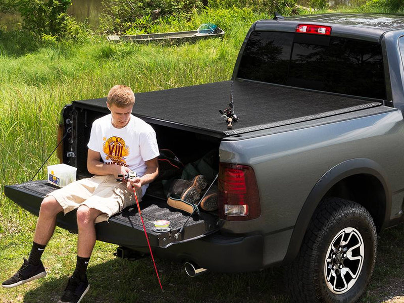 Man sitting on the lowered tailgate with fishing gear under the closed tonneau cover