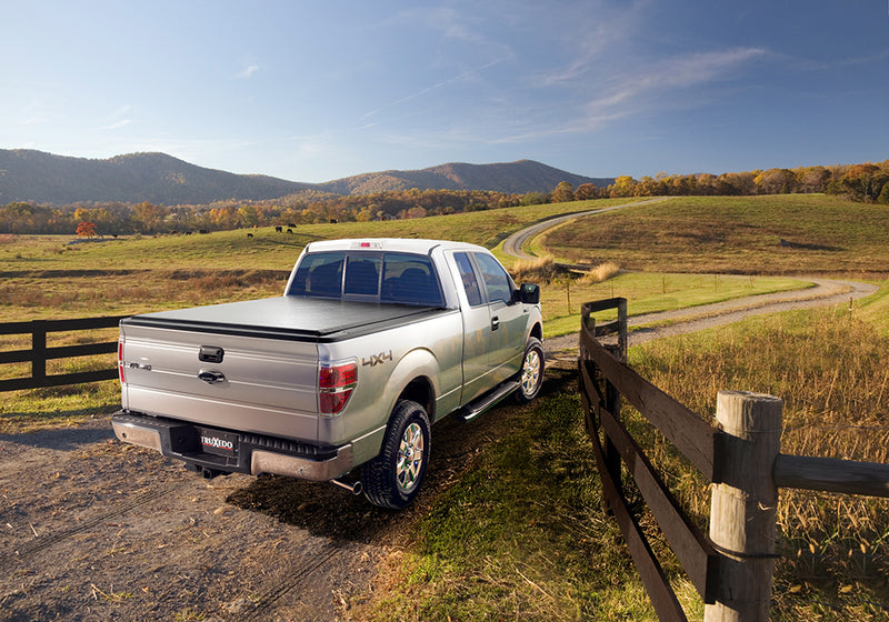 TruXedo Deuce soft folding tonneau cover closed on a 2009-2014 Ford F-150, rear three-quarter view, standing beside a timber fence with autumn hills beyond, photographed on location