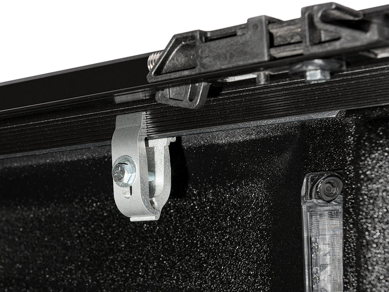 Close-up of the clamp bracket that grips the bed rail, seen from inside the bed beside the bed lamp on a TruXedo Deuce soft folding tonneau cover