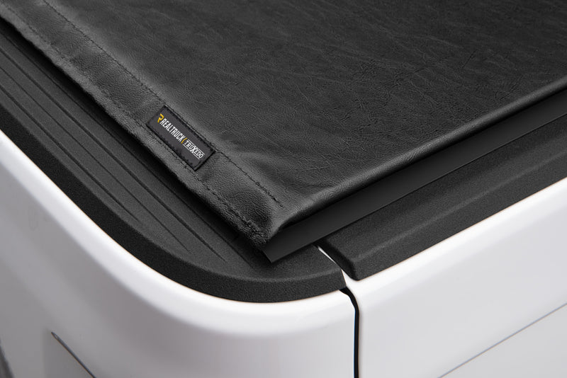 Close-up of the LO PRO name plate at the corner where the cover's rear edge meets the side rail on a TruXedo Lo Pro soft roll-up tonneau cover