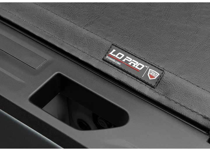 Close-up of the LO PRO name plate in tight macro beside the tailgate handle recess on a TruXedo Lo Pro soft roll-up tonneau cover
