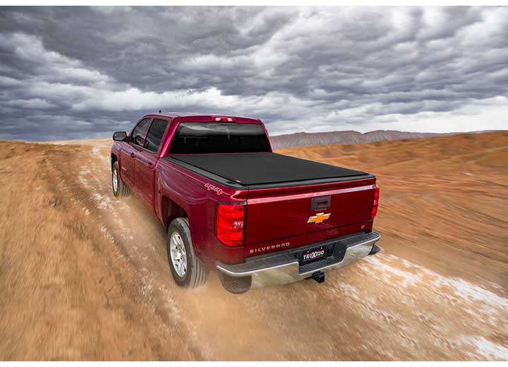TruXedo Pro X15 soft roll-up tonneau cover closed over the bed of a pickup truck, rear three-quarter view, on a dirt road under storm cloud, a photo-illustration rather than location photography, photographed on location