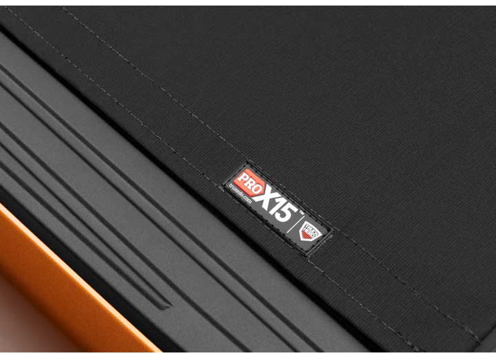 Close-up of the PRO X15 name plate on the cover's rear edge above an orange bedside on a TruXedo Pro X15 soft roll-up tonneau cover