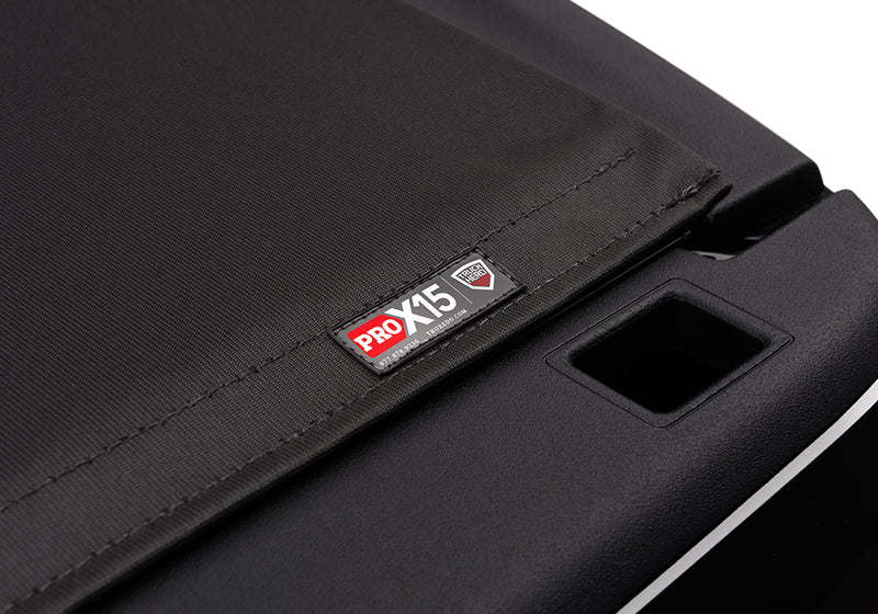 Close-up of the PRO X15 name plate on the cover's rear edge, above a chrome bedside trim strip on a TruXedo Pro X15 soft roll-up tonneau cover