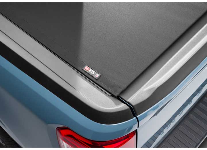 Close-up of the PRO X15 name plate at the far edge of the cover in a wide crop across a pale blue bedside on a TruXedo Pro X15 soft roll-up tonneau cover