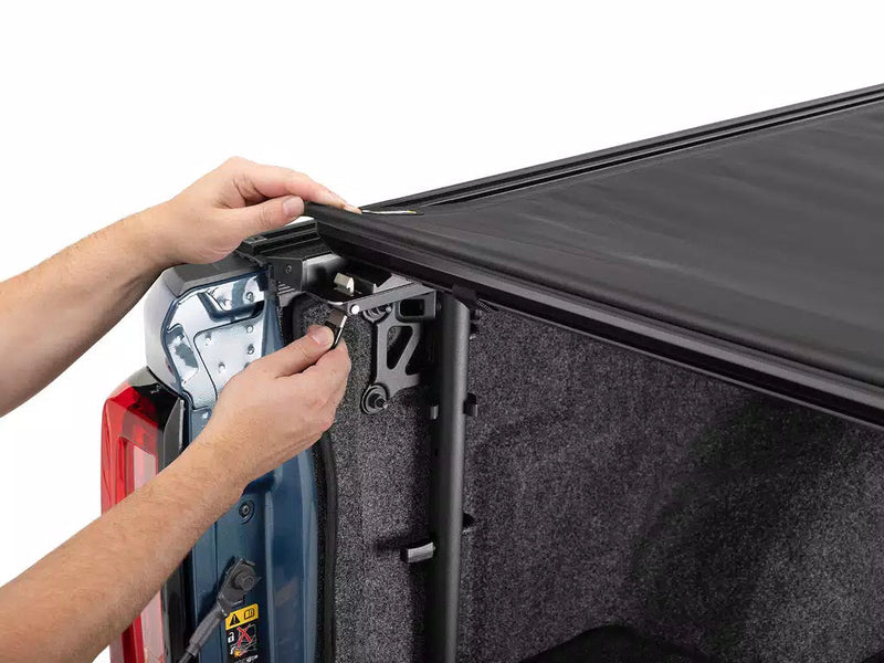 Hands adjusting the cover's latch hardware at the rear corner of the bed