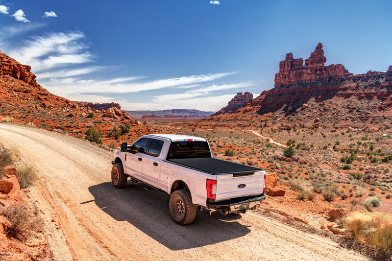 TruXedo Sentry CT hard roll-up tonneau cover closed over the bed of a pickup truck, rear three-quarter view, on a red-rock dirt road between sandstone buttes, photographed on location