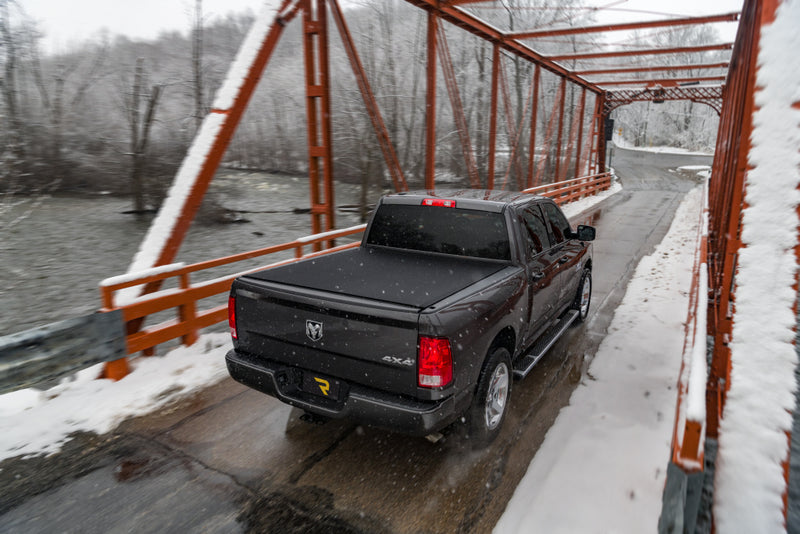 TruXedo Sentry CT hard roll-up tonneau cover closed over the bed of a pickup truck, rear three-quarter view, crossing a snow-covered steel truss bridge, photographed on location