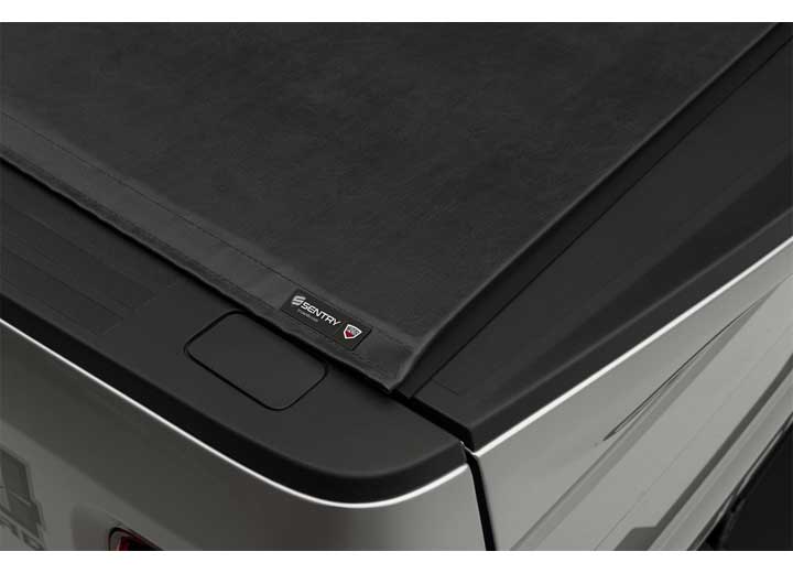 Close-up of the SENTRY name plate at the center of the cover's rear edge, above a silver bedside on a TruXedo Sentry hard roll-up tonneau cover