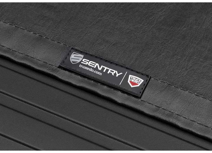 Close-up of the SENTRY name plate in tight macro, its truxedo.com line legible on a TruXedo Sentry hard roll-up tonneau cover