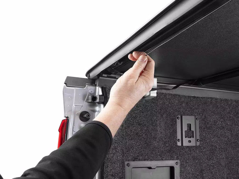 A hand pulling the rear edge of the TruXport cover over the open tailgate to latch it