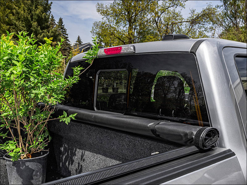 TruXport cover rolled and strapped at the cab with a potted shrub standing in the open bed at a garden center
