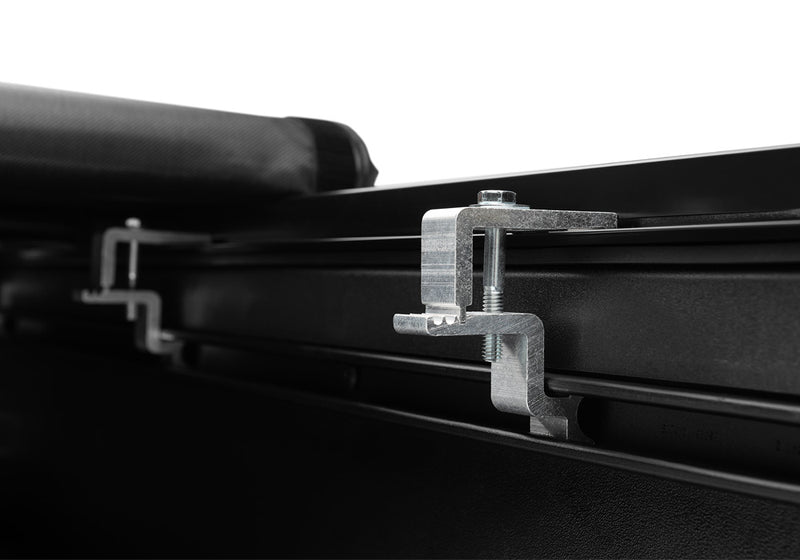 Close-up of the bed-rail clamp with the rolled cover resting on the rail above it on a TruXedo TruXport soft roll-up tonneau cover