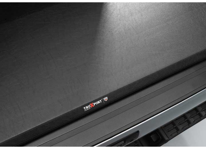 Close-up of the TRUXPORT name plate seen from above, a band of light across the cover on a TruXedo TruXport soft roll-up tonneau cover