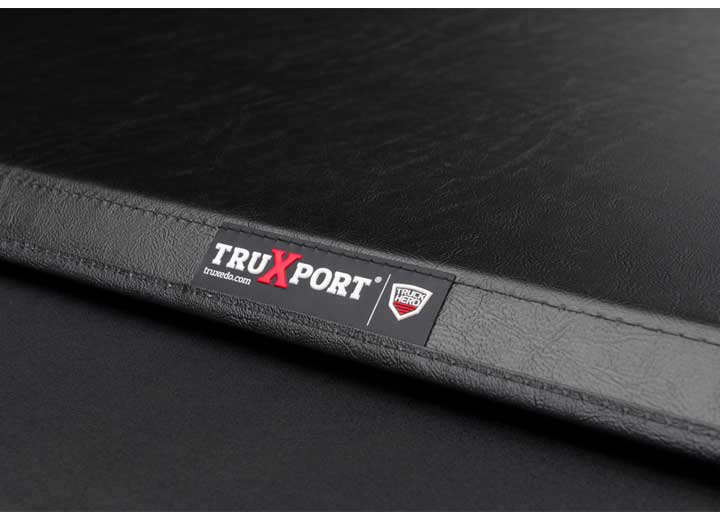Close-up of the TRUXPORT name plate viewed along the cover's rear seam from the corner on a TruXedo TruXport soft roll-up tonneau cover