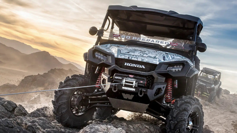 Warn AXON 45 winch mounted on a side-by-side working through rocky terrain, wire rope running over the roller fairlead