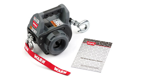 Warn Drill Winch in gray and black with the carry handle across the top, drill drive socket on the side, steel rope with a hook at each end and a red Warn strap, shown beside the Drill Winch operator's manual