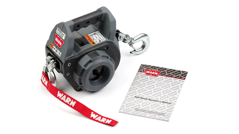 Warn Drill Winch in grey and black with the carry handle across the top, drill drive socket on the side, steel rope with a hook at each end and a red Warn strap, shown beside the Drill Winch operator's manual