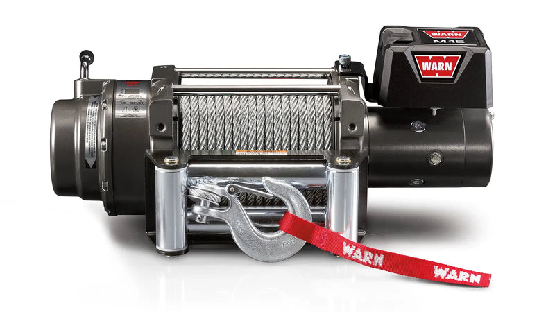 Warn M15 winch, front elevation on white, showing the large-frame body, 7/16" wire rope on the drum, roller fairlead, latched hook with red Warn strap and the control pack badged M15