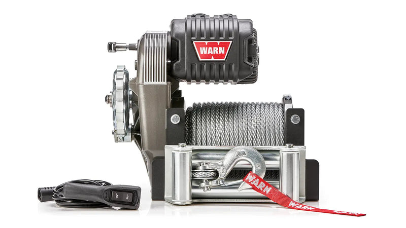 Warn M8274 winch, front elevation on white, showing the upright frame, steel rope on the drum, roller fairlead, clevis hook with red Warn strap, and the wired remote