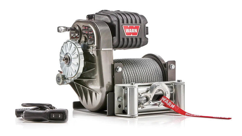 Warn M8274 winch, three-quarter view on white, showing the free-spool clutch dial, the gearbox decal panel, the control pack and steel rope on the drum