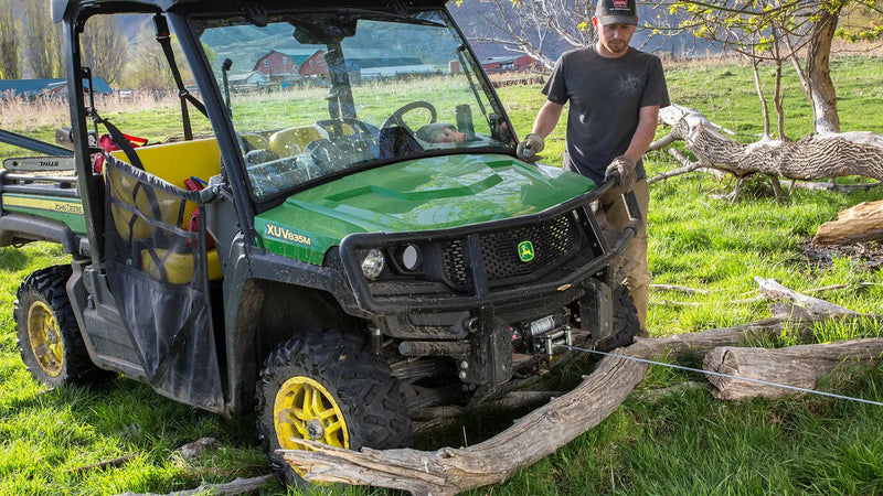 A Warn VRX series steel-rope winch in use on a utility machine, wire rope running over a roller fairlead to a log