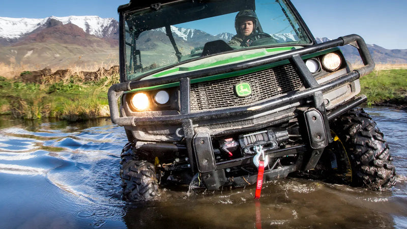 Warn VRX 45-S powersports winch mounted on a utility side-by-side crossing a shallow river, synthetic rope running out to an anchor