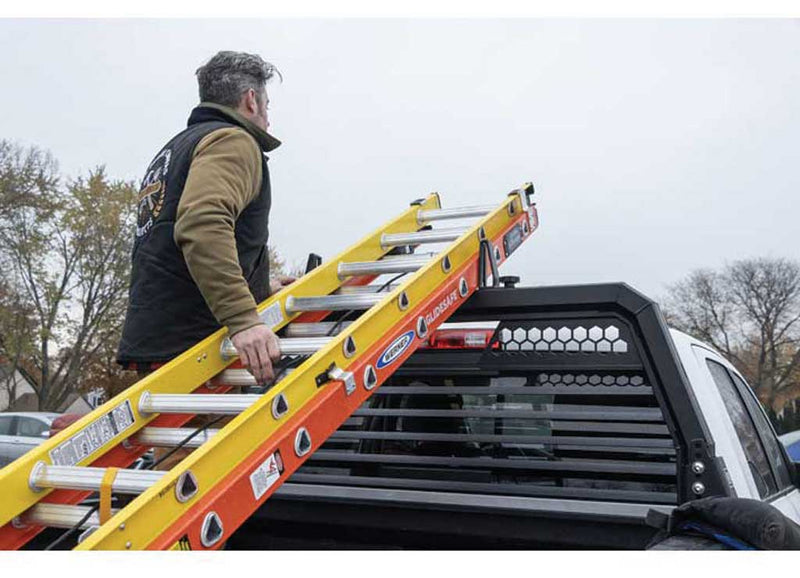 Worker sliding an extension ladder onto the Weather Guard louvered headache rack at a jobsite