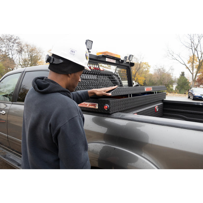 Worker in a hard hat reaching into a truck bed with the Weather Guard hex headache rack fitted behind the cab