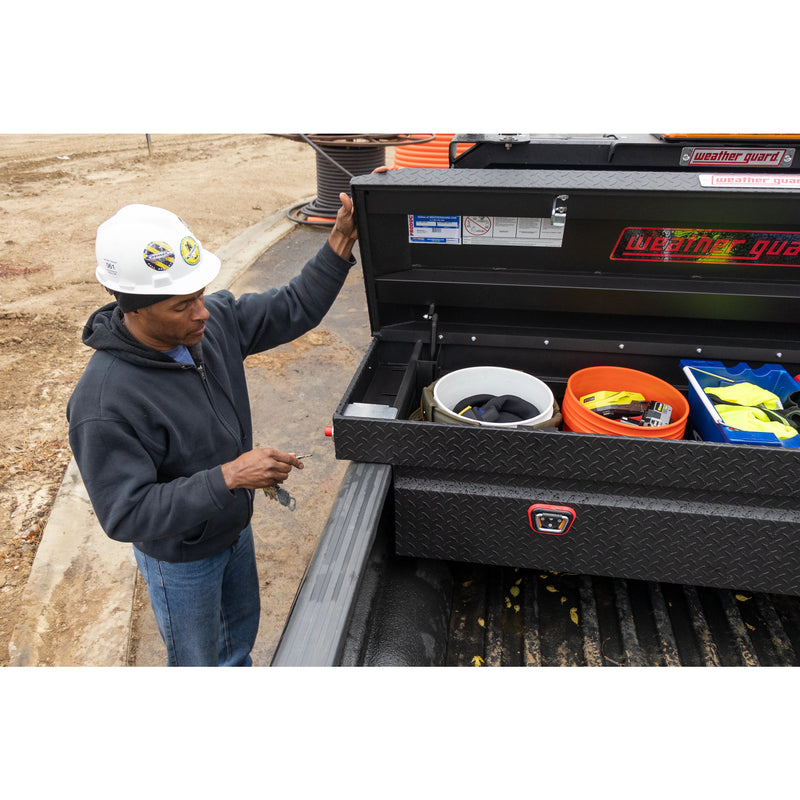 Weather Guard 127-52-04 crossover saddle box in textured matte black, in use on a truck bed with a technician reaching into the open box