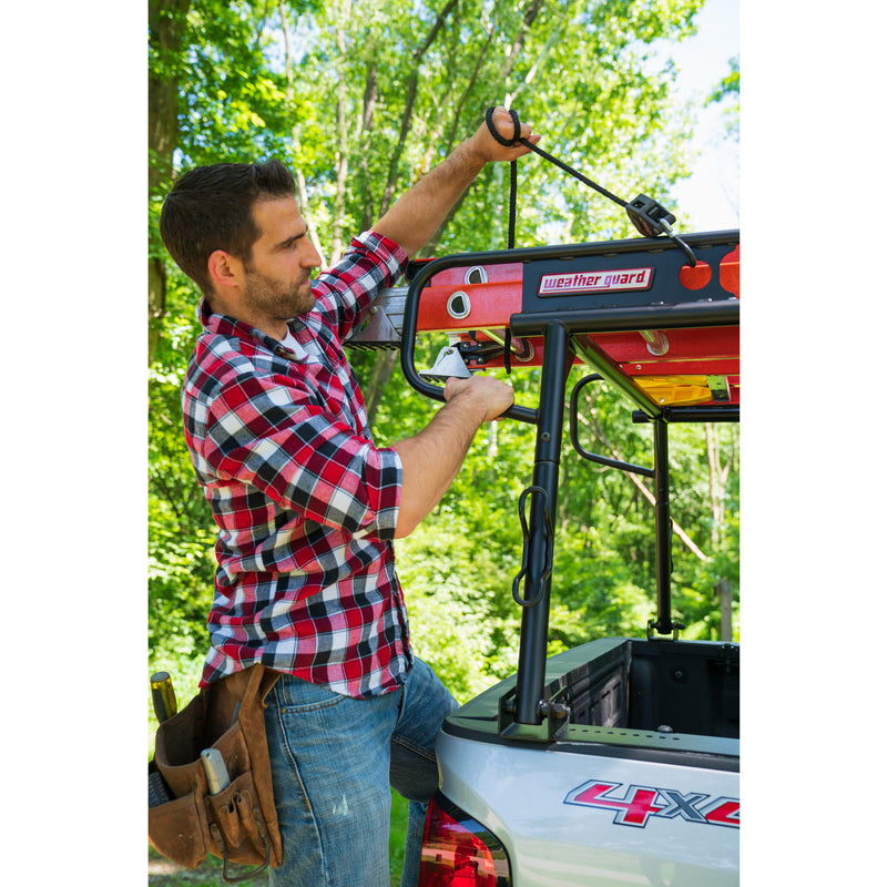 Worker tightening a ratchet tie-down over a ladder on the Weather Guard compact truck rack