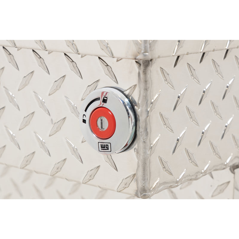 Weather Guard 137-0-04 crossover saddle box in bright aluminum diamond plate, close-up of the red push-button lock and Weather Guard badge