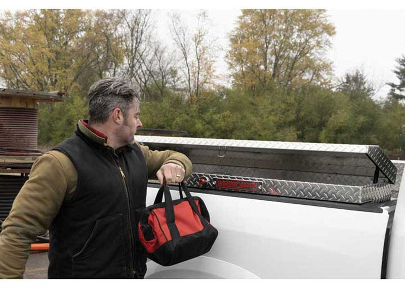 Weather Guard 178-0-04 low-profile Lo-Side box in bright aluminum diamond plate, in use as a worker lifts a tool bag out of the open box in a white Ram bed