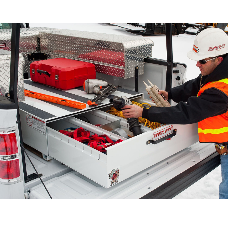 Worker in a hard hat and safety vest reaching into an open Weather Guard Pack Rat drawer full of tools in a snowy truck bed