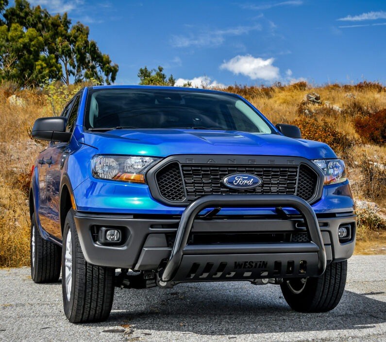 Westin E-Series 3 inch bull bar in black finish with skid plate installed on the front of a blue Ford Ranger parked on a gravel road with dry hills behind