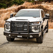 Three quarter angle view of the black Westin HDX Bandit front bumper and grille guard installed on a white Chevrolet Silverado HD parked on gravel