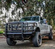 Black Westin HDX Bandit front bumper with diamond plate face and grille guard installed on a lifted silver Ford Super Duty pickup truck under trees