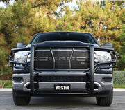 Front view of a black Westin HDX grille guard with HDX badge mounted on a black Ram pickup truck with trees behind it