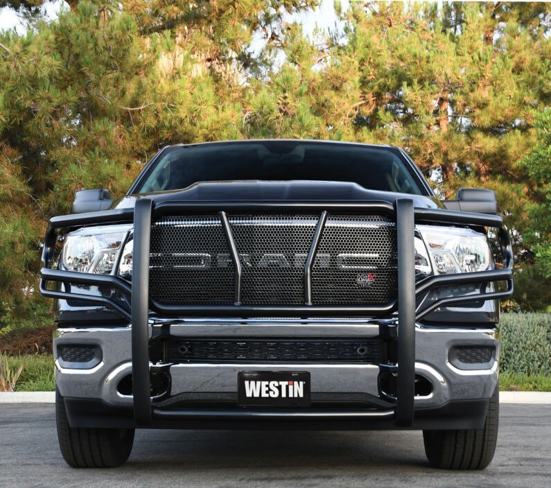 Front view of a black Westin HDX grille guard with HDX badge mounted on a black Ram pickup truck with trees behind it