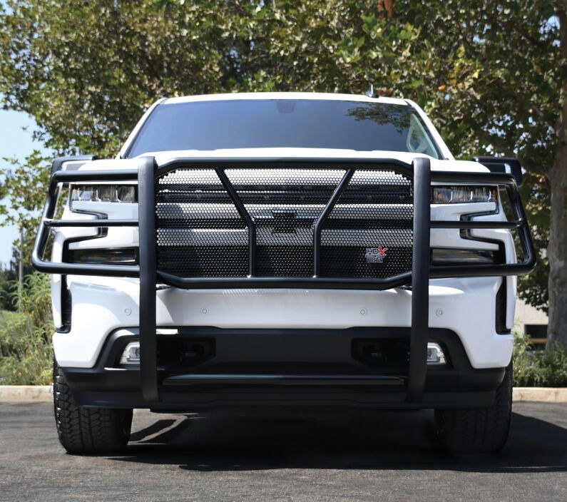 Head-on view of a black Westin HDX grille guard with mesh insert fitted to a white Chevrolet Silverado pickup parked outdoors