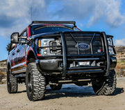 Black textured Westin HDX grille guard installed on a lifted black Ford Super Duty pickup parked on dirt under a blue sky
