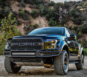 Westin Outlaw front off-road bumper in textured black finish with an LED light bar installed on a blue Ford F-150 Raptor parked on a gravel trail