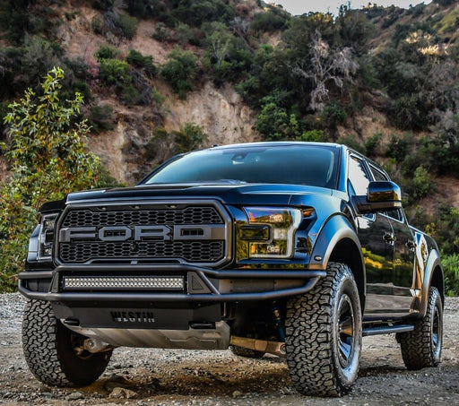 Westin Outlaw front off-road bumper in textured black finish with an LED light bar installed on a blue Ford F-150 Raptor parked on a gravel trail